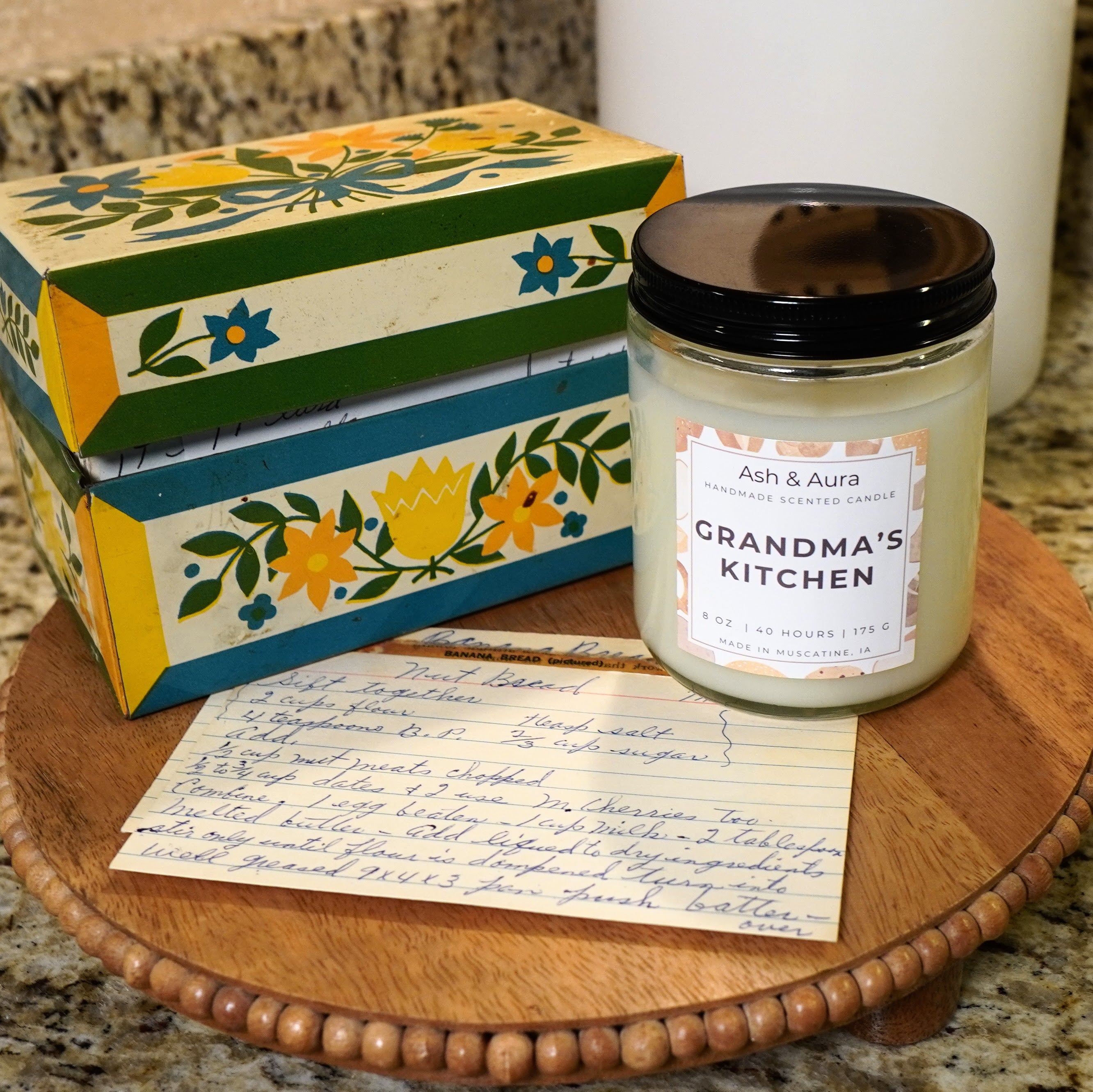 An unlit Grandma's Kitchen candle in a kitchen setting, next to a recipe for banana nut bread.